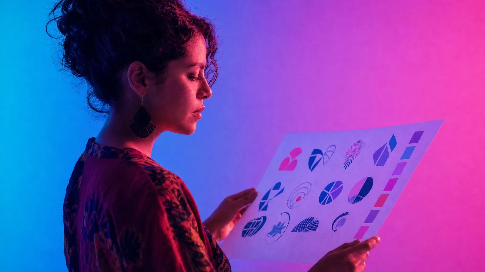 Diseñadora revisando una hoja de propuestas de logo bajo luz cian, violeta y rosa